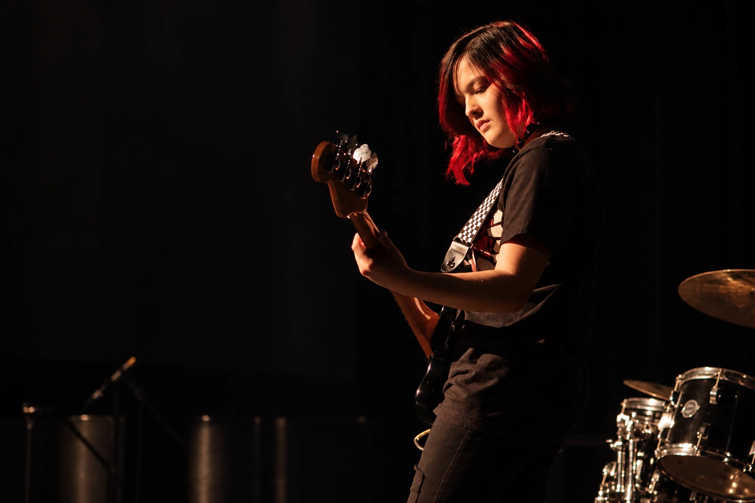 Bass guitarist with a checkerboard strap performing under red stage lighting